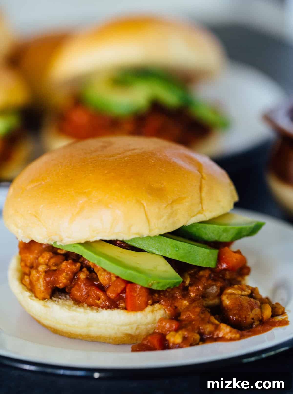 These pumpkin BBQ sloppy joes are going to be your new favorite weeknight recipe! They're a quick dinner idea filled with loads of flavor. Two pumpkin BBQ sloppy joes sandwiches garnished with avocado slices, overflowing from their buns on a plate, with a background of more sloppy joes.