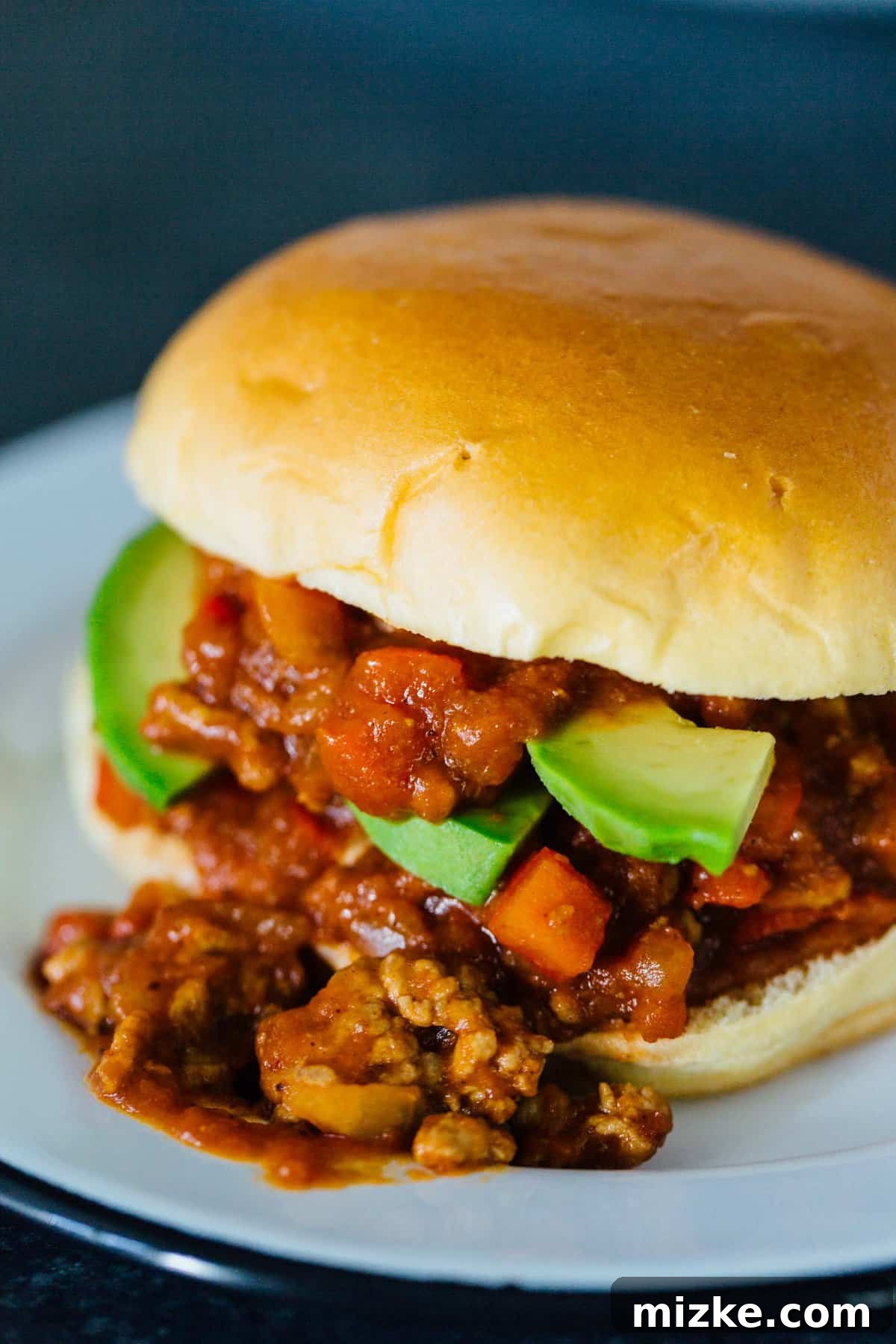 These pumpkin BBQ sloppy joes are going to be your new favorite weeknight recipe! They're a quick dinner idea filled with loads of flavor. A pumpkin BBQ sloppy joes sandwich overflowing from its bun, garnished with avocado slices on a white plate.