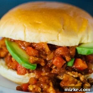 A pumpkin BBQ sloppy joes sandwich garnished with avocado slices, spilling out of the bun on a plate.