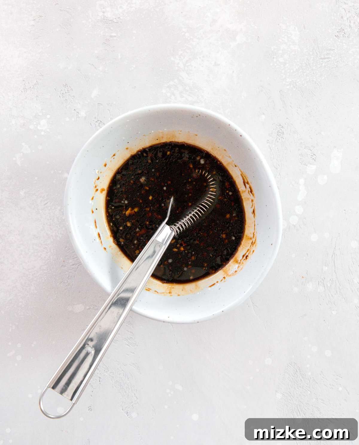 The perfectly whisked sauce for Chinese Chicken and Broccoli, ready to bring rich flavor to your dish. Chinese Chicken and Broccoli sauce expertly whisked together in a white speckled bowl, showcasing its smooth consistency.