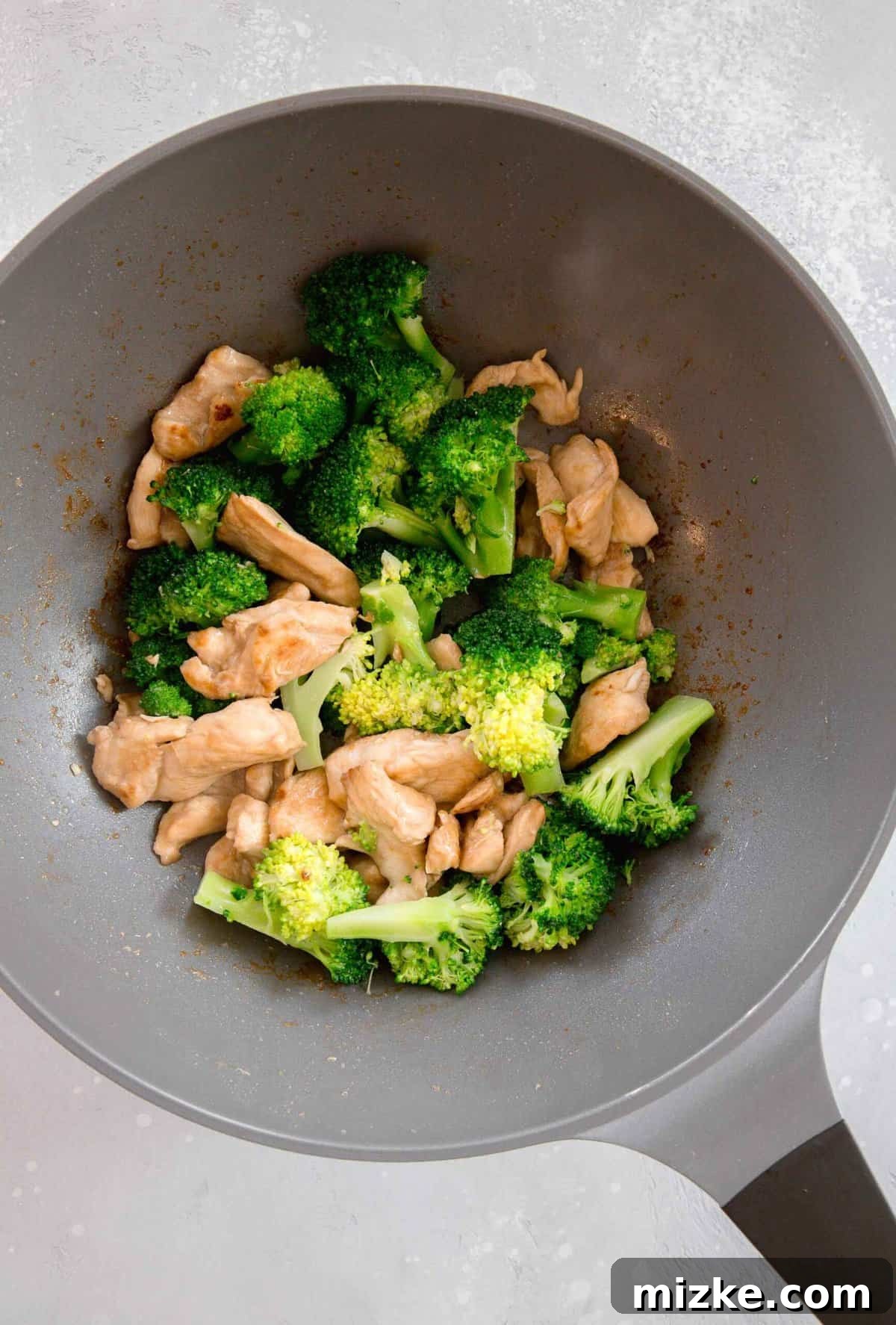 Combining crisp broccoli with browned chicken in the wok for a flavorful Chinese stir-fry. Drained broccoli florets added to the wok alongside the beautifully browned chicken, ready to be tossed in sauce.