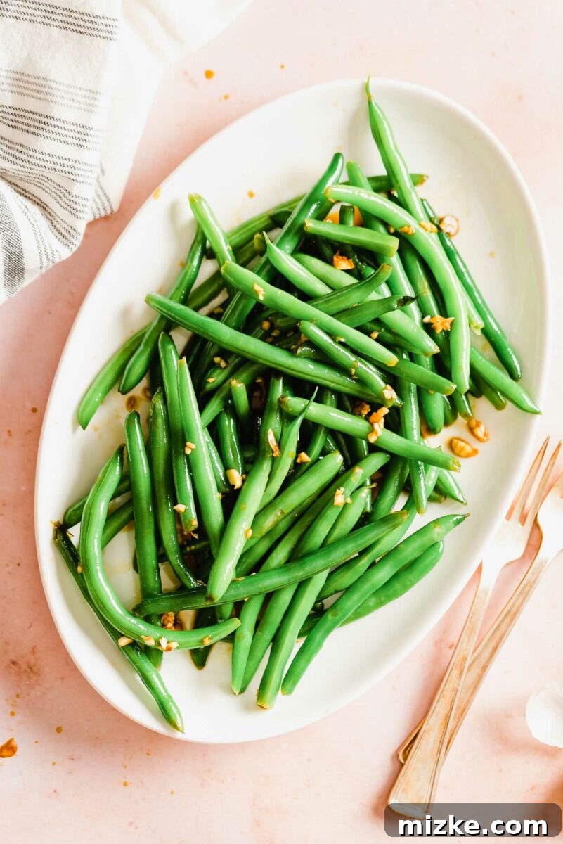 An oval-shaped white plate is filled with a neatly piled serving of exquisitely marinated green beans, highlighting their vibrant color.
