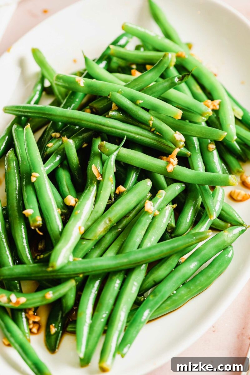 A close-up shot of a white plate generously laden with glistening garlic and soy green beans, showcasing their rich marinade.