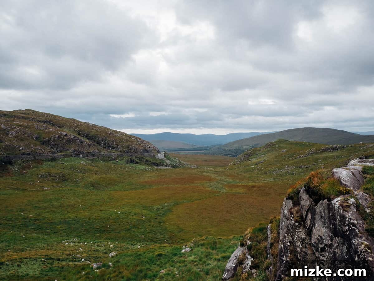 Killarney: Ireland's Emerald Gem 3 Vast green mountainous landscape with a winding road leading towards a distant lake, Ireland