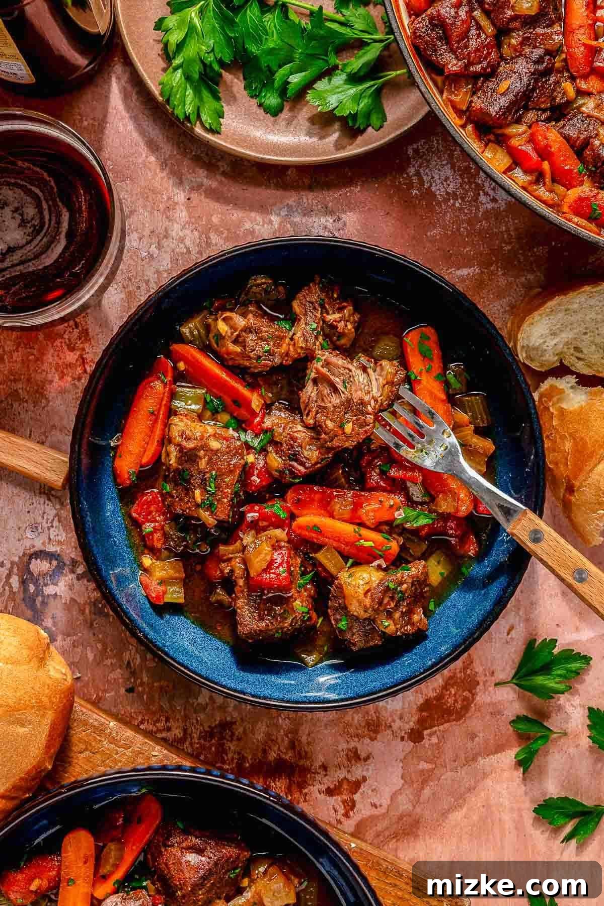 Hearty Ale Braised Beef 3 A generous bowl of beer braised pot roast, showcasing succulent, tender chunks of beef, vibrant carrots, and fresh herbs. The dish is beautifully garnished with freshly chopped parsley, adding a pop of green. Surrounding the rustic bowl are perfectly toasted slices of crusty bread, a small bundle of fresh parsley, and a glass of elegant red wine, all arranged on a textured wooden table to create a warm and inviting rustic dining scene.