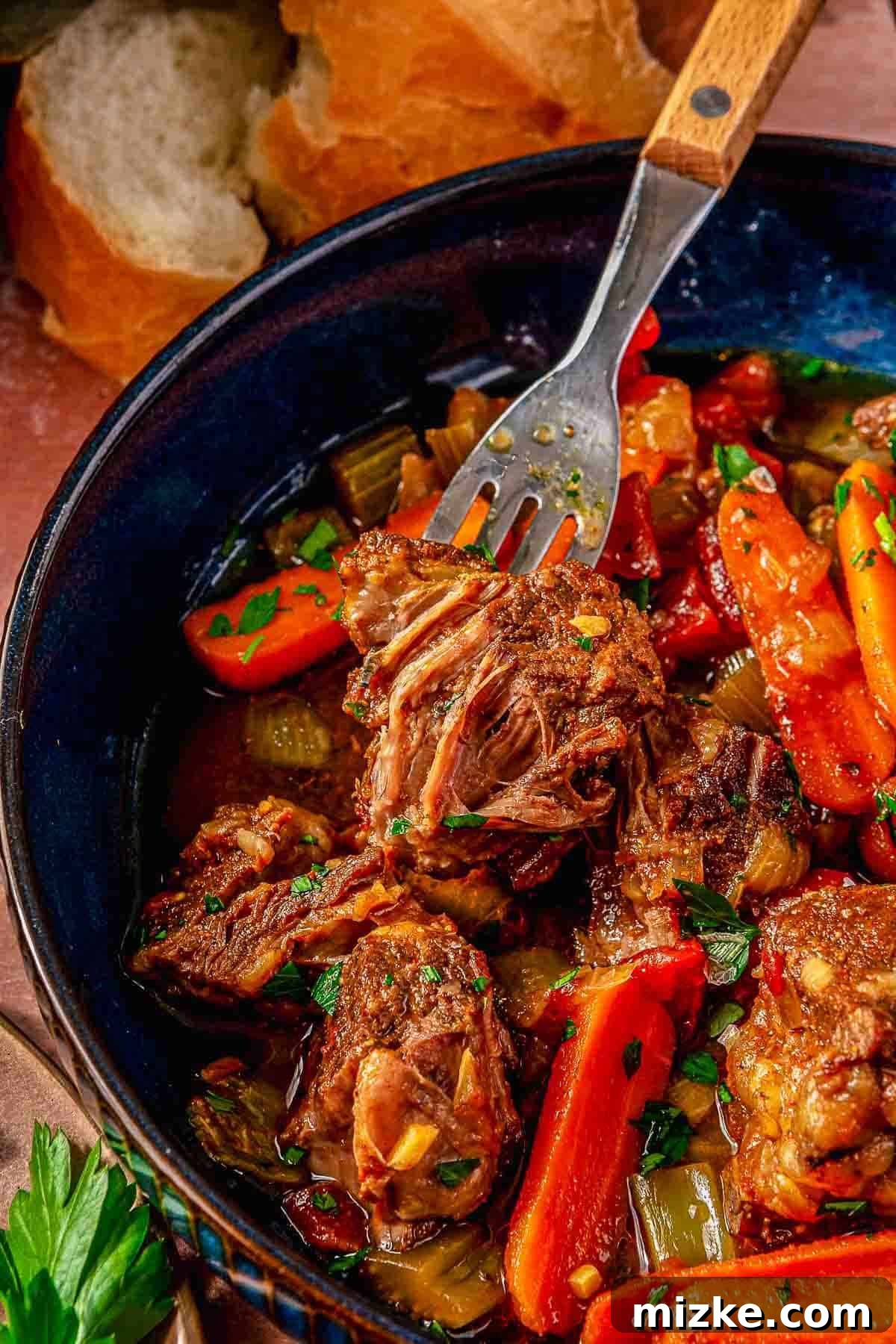 Hearty Ale Braised Beef 4 A vibrant close-up of a beer braised pot roast presented in a charming blue bowl. The image highlights perfectly tender chunks of rich beef and bright, sweet carrots, creating an inviting visual contrast. The dish is elegantly garnished with fresh herbs, enhancing its aromatic appeal. In the softly blurred background, slices of rustic bread are visible, completing the warm and hearty presentation of this comforting meal.