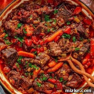 A savory beer braised pot roast in a green pot, filled with chunks of beef, carrots, tomatoes, and herbs. A wooden spoon rests on the side. Fresh parsley is scattered on top, and a glass of red wine and a bunch of parsley are beside the pot.