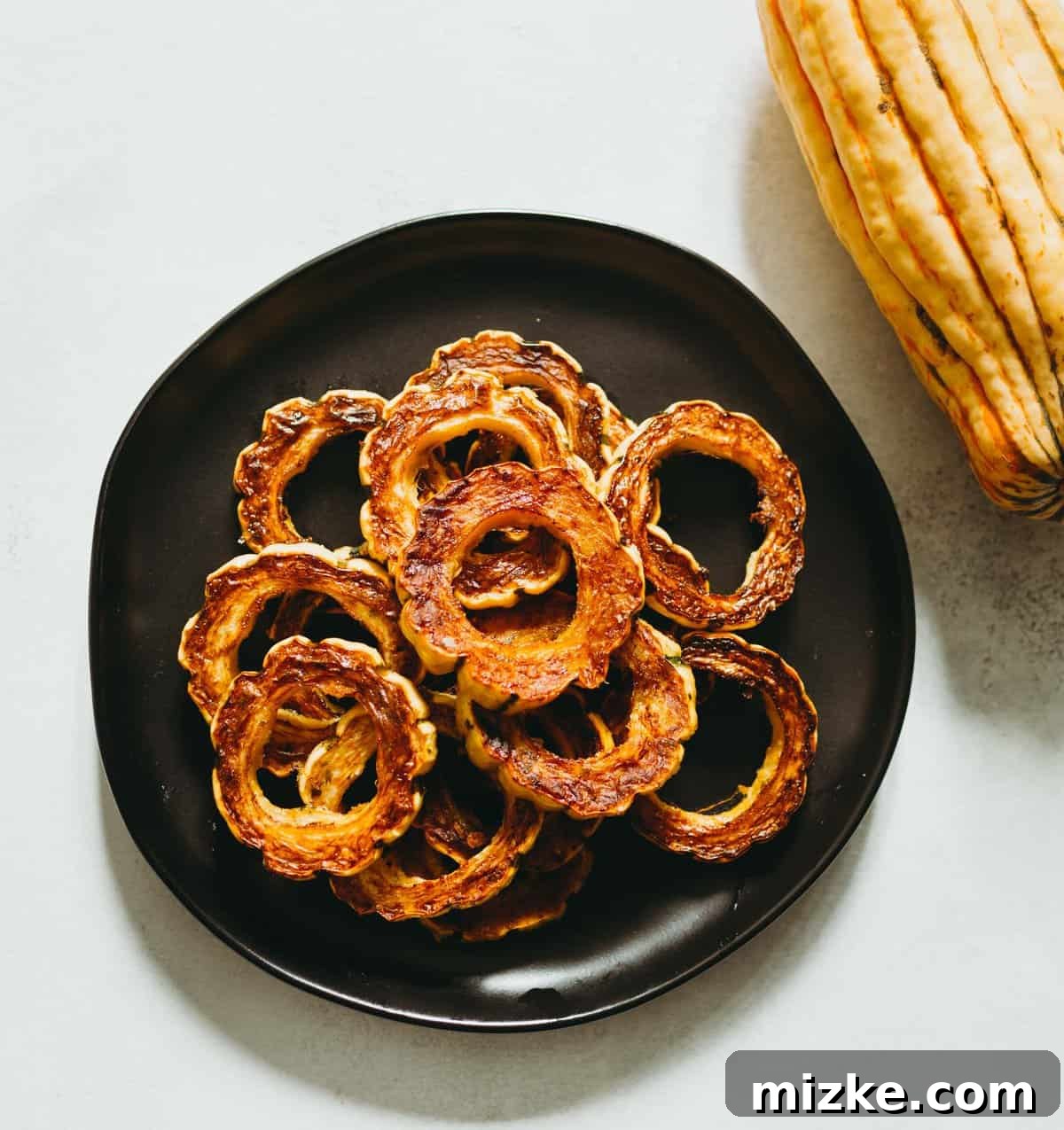 Caramelized Delicata Squash 4 Overhead view of glistening roasted delicata squash rings on a dark plate, garnished with fresh herbs.