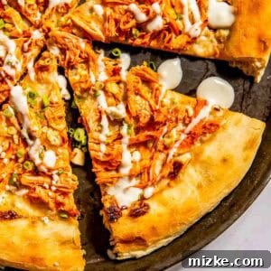 A pizza topped with shredded buffalo chicken, sliced green onions, and a drizzle of white sauce, cut into slices on a round pan.