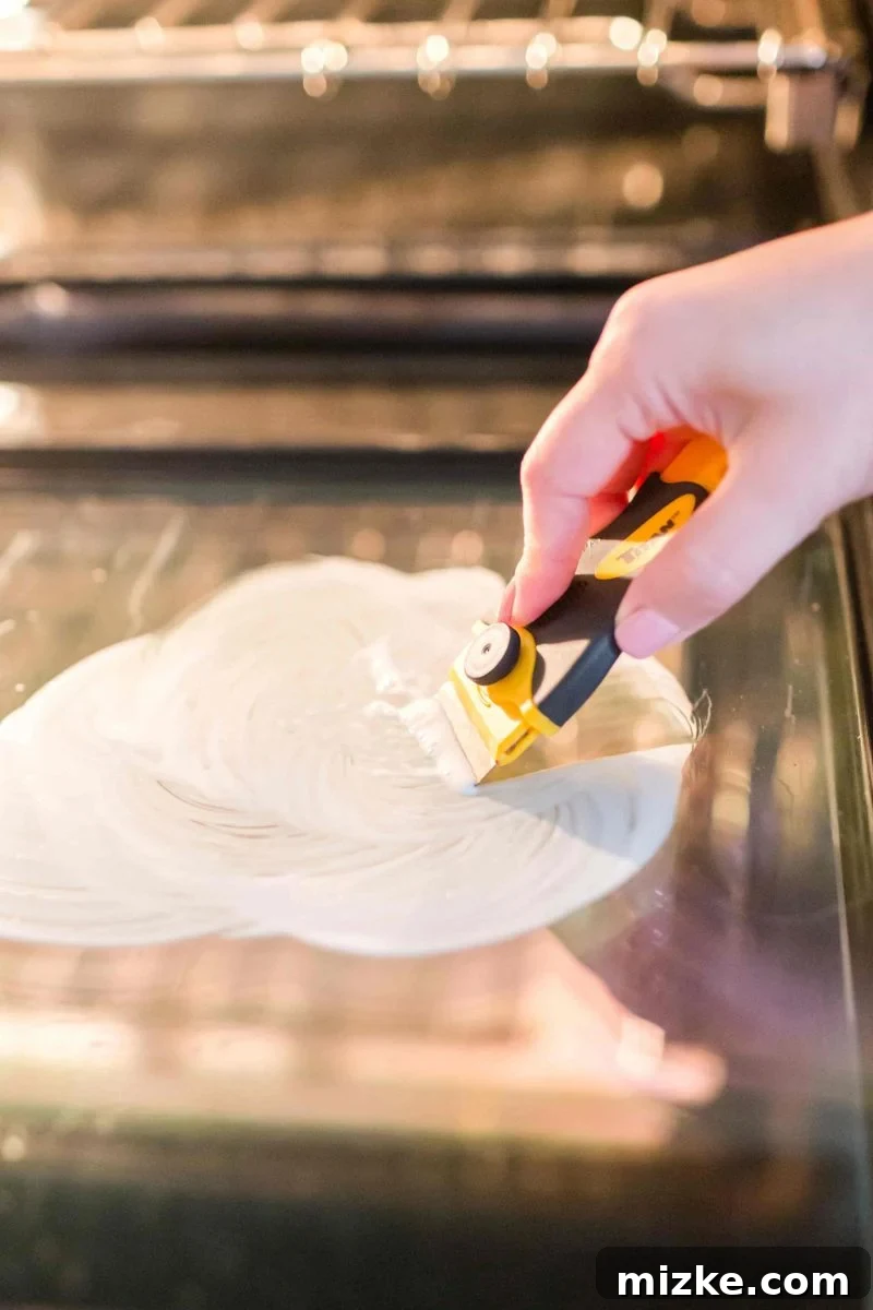 Spreading Bar Keepers Friend on the oven door with a soft sponge, preparing it for the deep cleaning process. Spread Bar Keepers Friend evenly across the glass oven door with a soft sponge, allowing it to sit and penetrate baked-on grime before scraping.