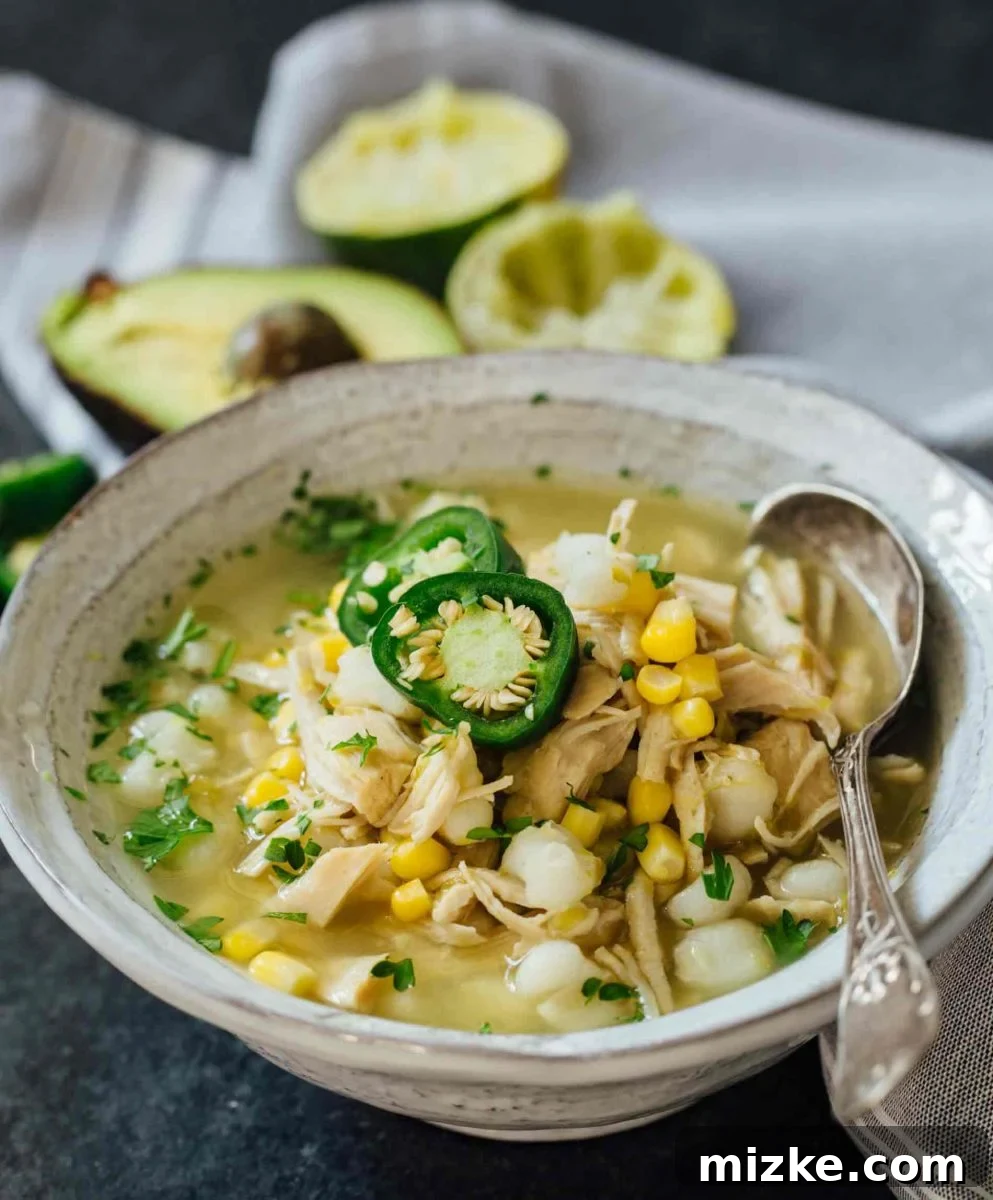 This Instant Pot jalapeño lime chicken soup is beyond flavorful! The spicy broth has hearty additions of hominy, corn, and shredded chicken. Put this all together in less than an hour! A close-up of a steaming bowl of Instant Pot Jalapeño Lime Chicken Soup, showcasing its rich broth, shredded chicken, and vibrant ingredients like corn and hominy.