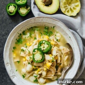 Instant Pot jalapeño lime chicken soup in a white bowl with metal spoon next to jalapenos, limes, and avocados