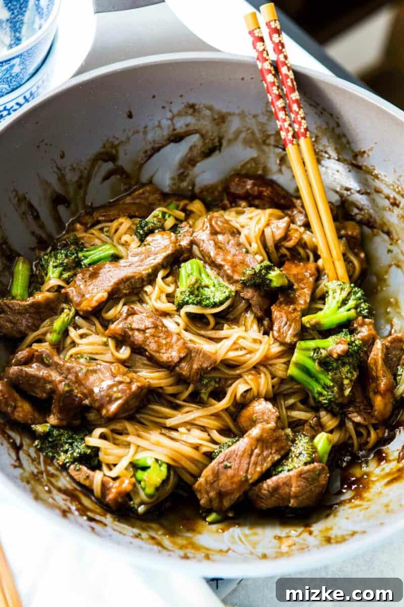 Close-up of a steaming bowl of Asian Beef and Broccoli Noodles, showcasing perfectly cooked beef and vibrant green broccoli against a backdrop of rice noodles, drenched in a glossy, dark sauce. A truly irresistible dish for any occasion.