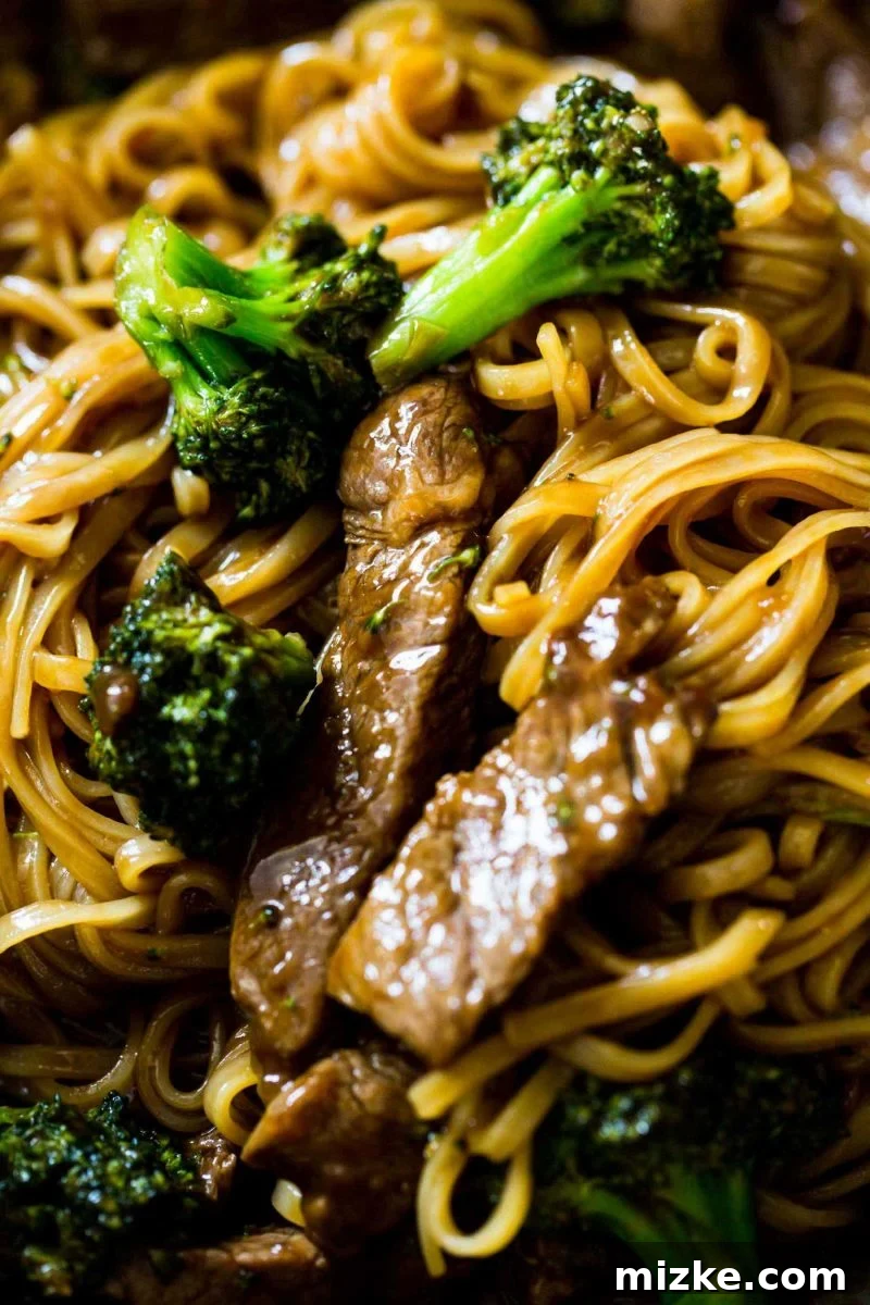 A close-up of the Asian Beef and Broccoli Noodles in a skillet, with the thick, glossy sauce perfectly coating every strand of noodle and piece of beef and broccoli. A visual feast for any noodle lover.
