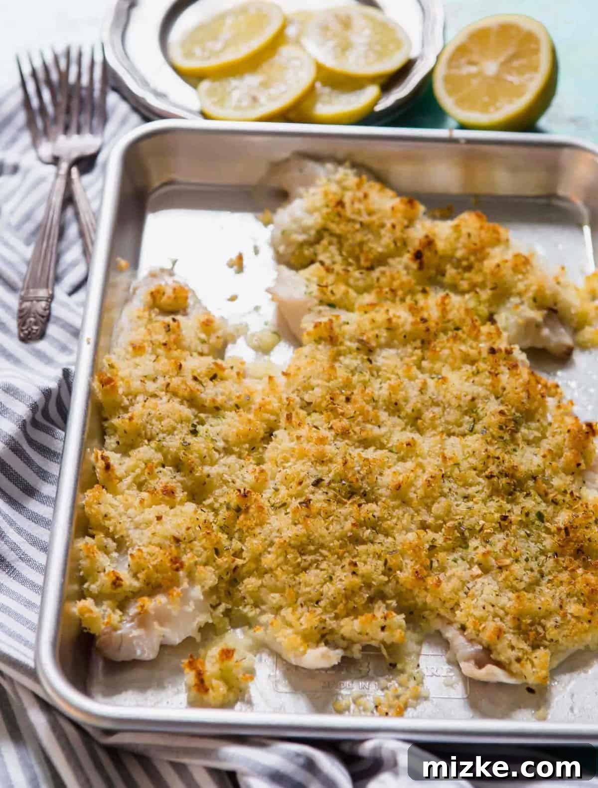 Crispy baked haddock on a sheet pan with two forks and lemon slices in background, ready to be served