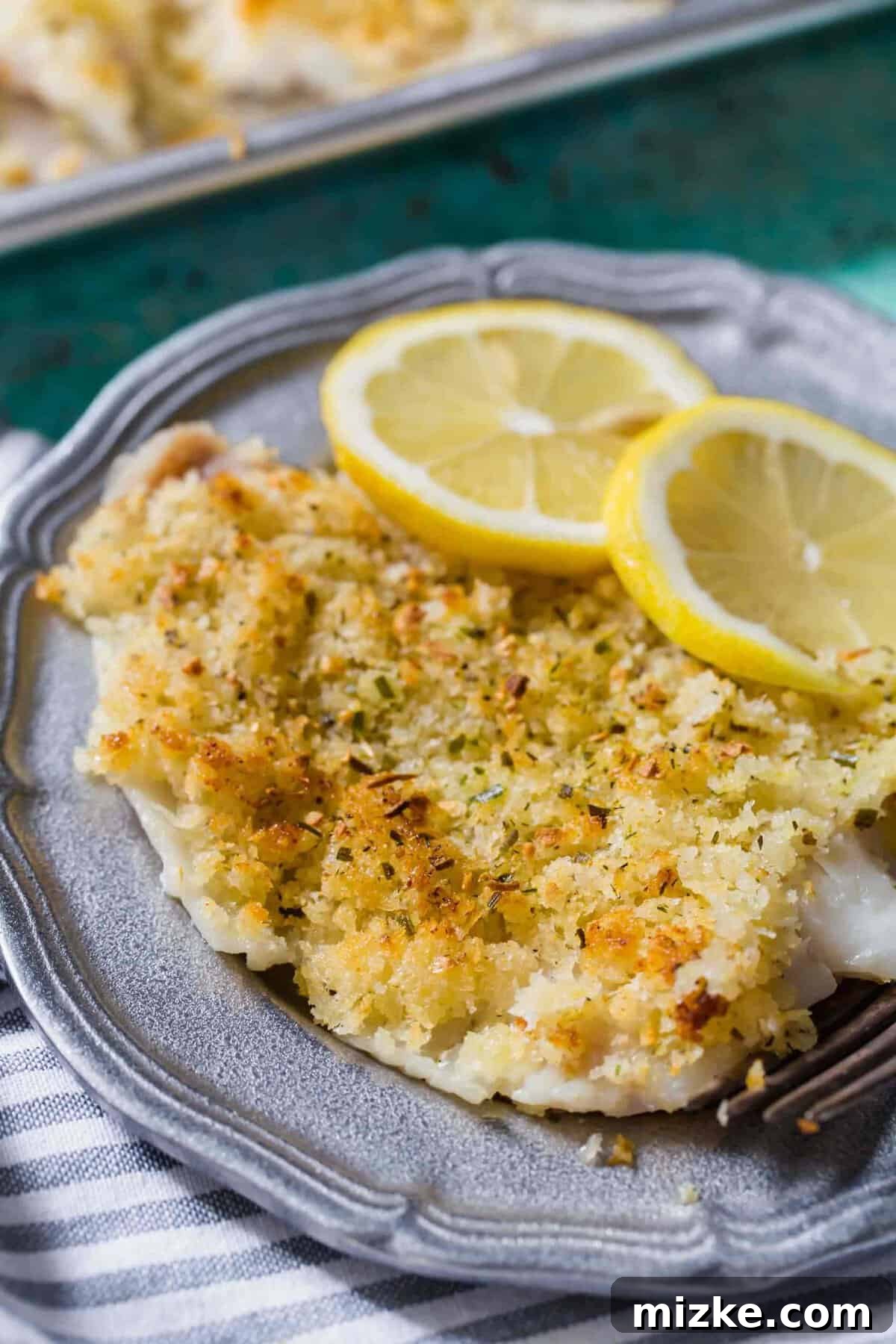 Baked haddock served on a white plate with fresh lemon slices and green garnish