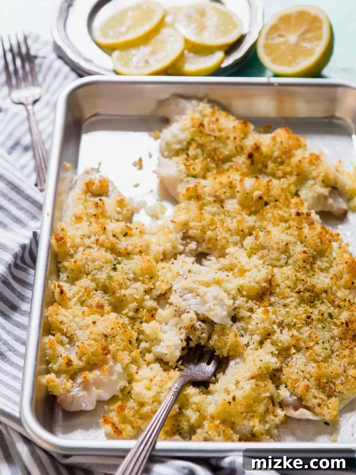 Crispy baked haddock on a baking sheet, fresh from the oven, with a fork gently flaking a piece