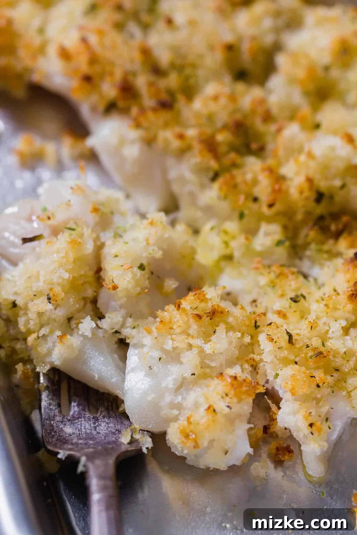 Close-up view of a piece of crispy, flaky haddock on a fork, highlighting its perfect crust and tender interior