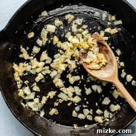 onions and garlic sautéed in a cast iron skillet with a wooden spoon