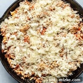 shredded mozzarella cheese and parmesan cheese sprinkled on top of pasta in cast iron skillet