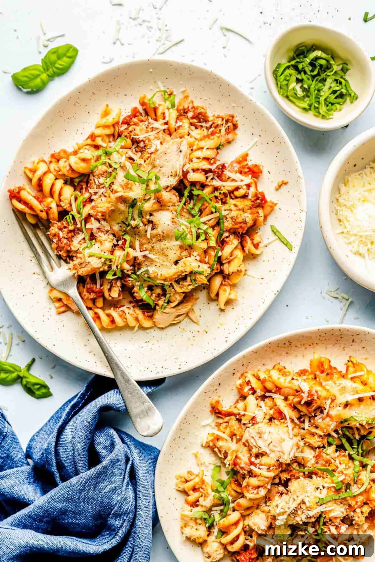 Cheesy Tuna Pasta Casserole 3 Two plates laden with generous portions of tuna pasta bake, garnished with fresh basil, accompanied by a metal fork and small bowls of fresh basil and Parmesan cheese.