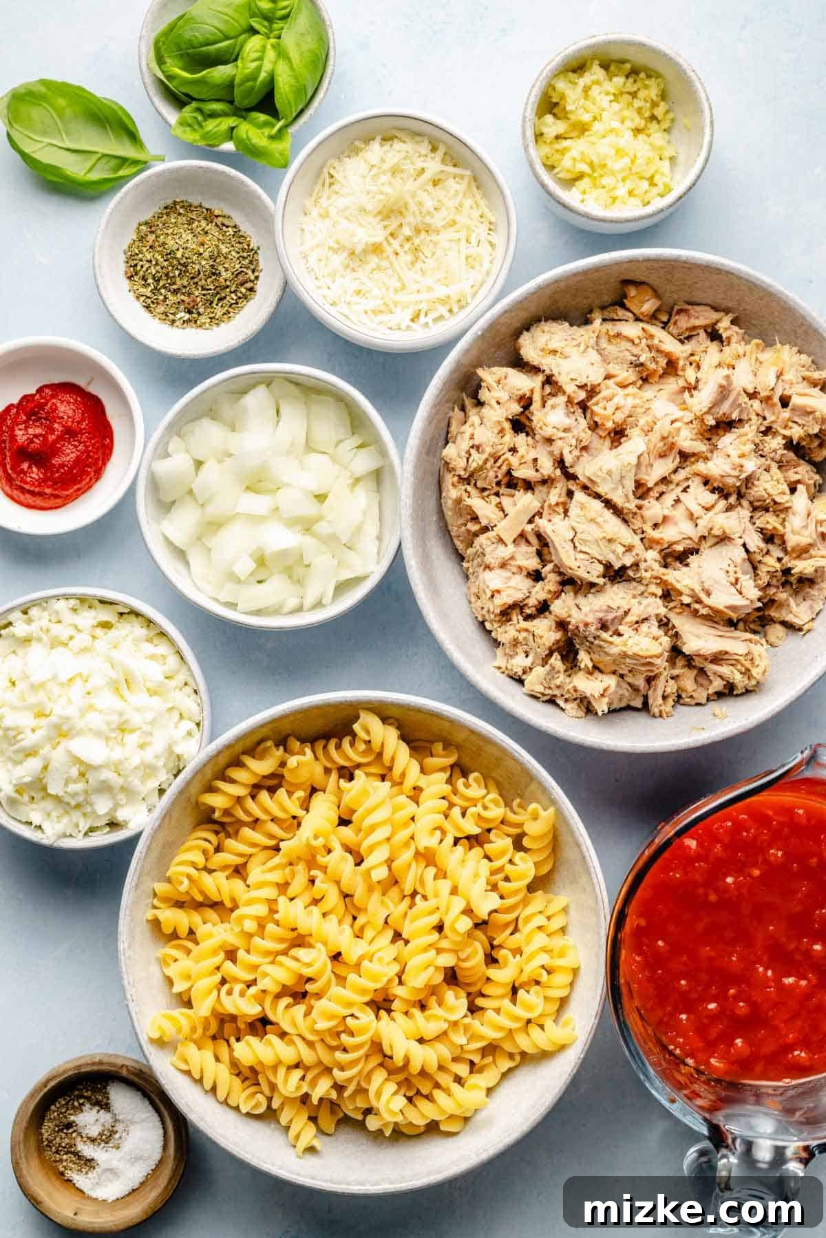 Cheesy Tuna Pasta Casserole 4 A collection of fresh ingredients for tuna pasta bake, including fusilli pasta, a can of tuna, tomatoes, onions, garlic, and various cheeses, neatly arranged on a countertop.