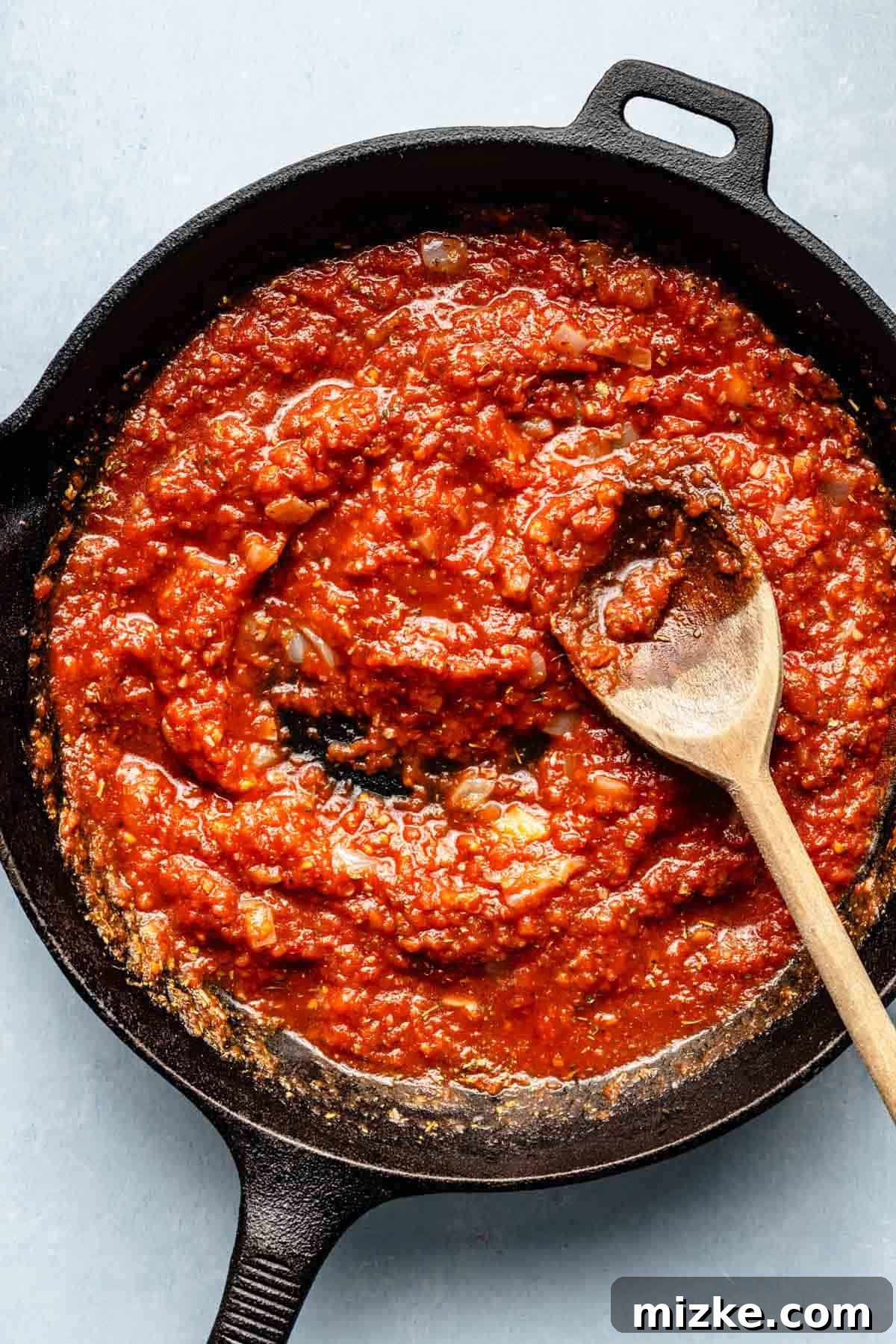 Cheesy Tuna Pasta Casserole 6 Rich red tomato sauce simmering in a cast iron skillet, infused with aromatics and seasonings, stirred gently with a wooden spoon.