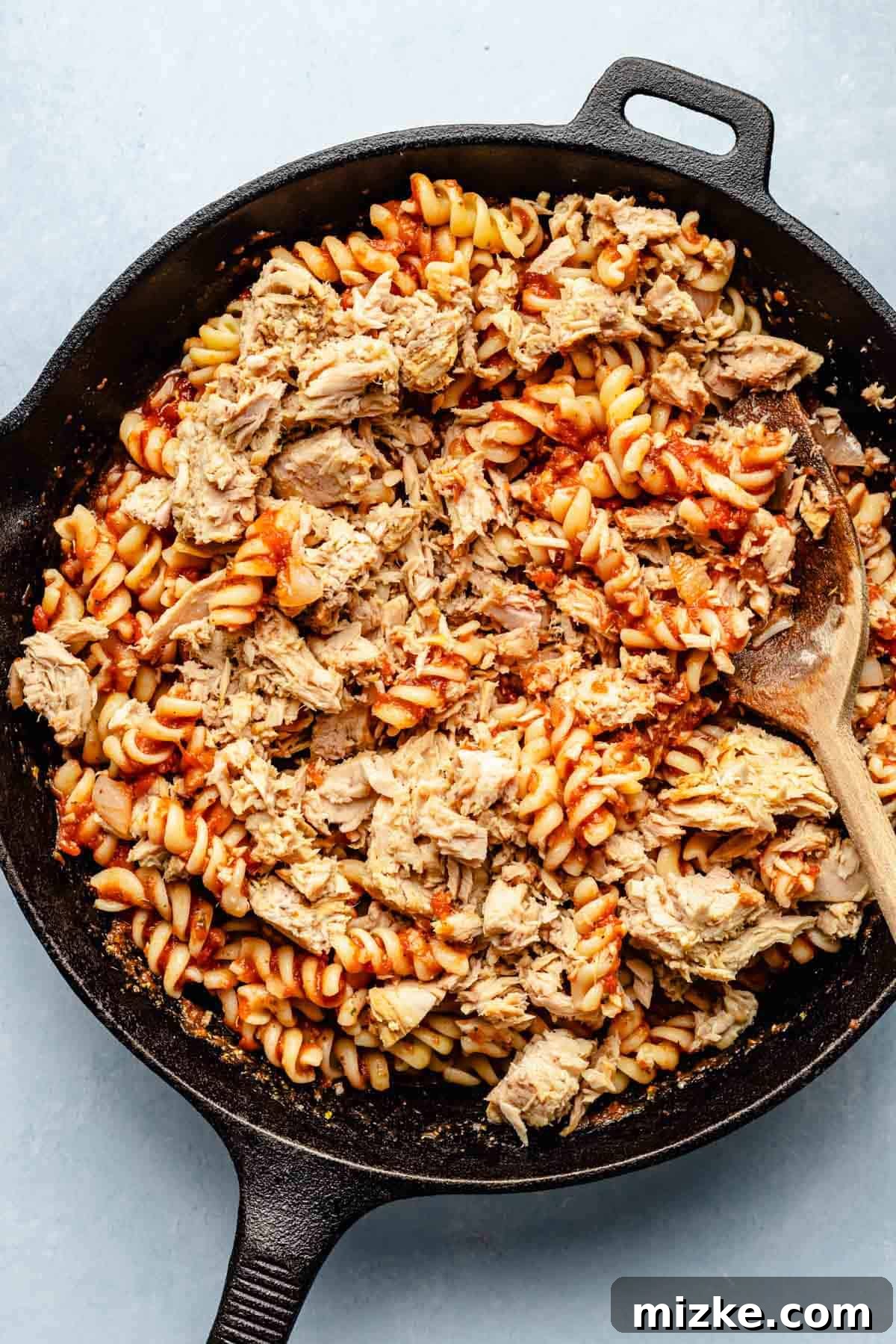 Cheesy Tuna Pasta Casserole 7 Partially cooked pasta and chunks of drained canned tuna being gently folded into the rich tomato sauce in a cast iron skillet.