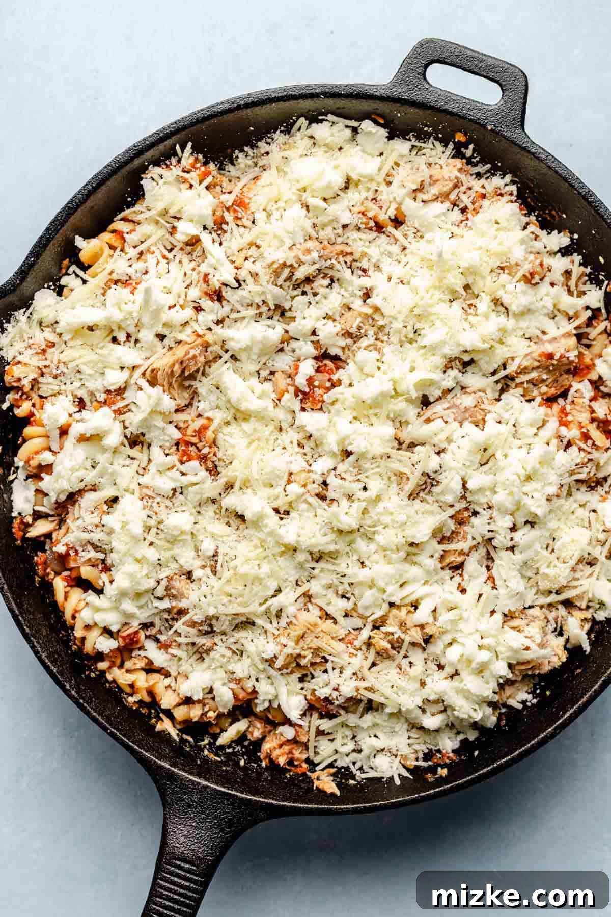 Cheesy Tuna Pasta Casserole 8 A generous layer of shredded mozzarella and grated Parmesan cheese sprinkled over the tuna pasta mixture in a cast iron skillet, ready for baking.