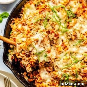 A wooden spoon scooping out a portion of the baked tuna pasta from a cast iron skillet, showcasing the melted cheese and hearty mixture.