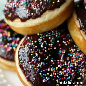 A stack of perfectly baked chocolate glazed donuts with colorful sprinkles.