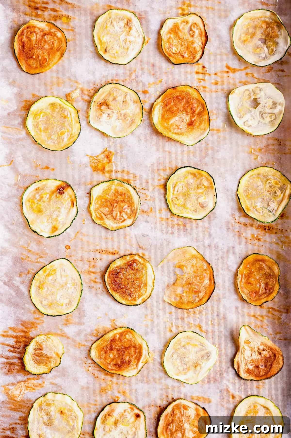 Simple Golden Zucchini Crisps 4 Overhead view of thinly sliced zucchini chips arranged on a parchment-lined baking sheet