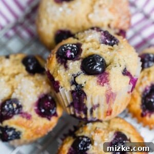 A close-up of a golden-brown blueberry muffin, showing a perfect rise, sparkling sugar on top, and abundant blueberries within the moist crumb.