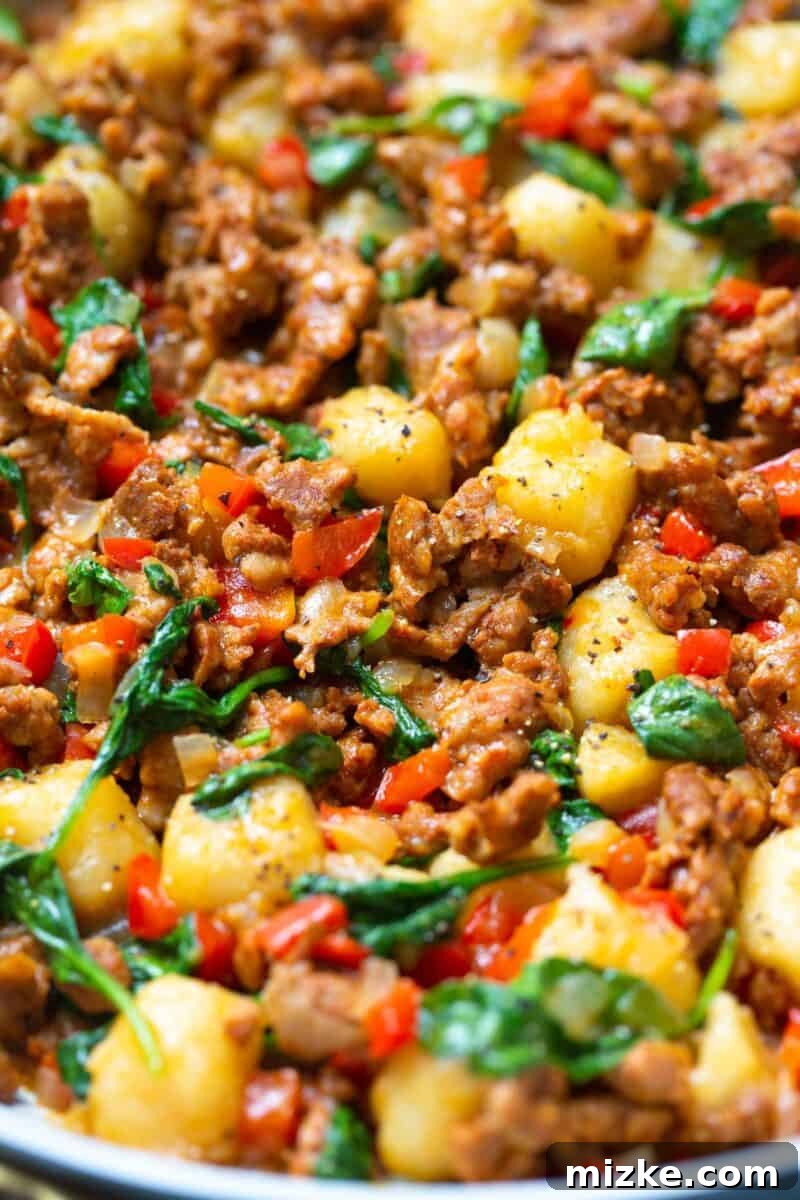 A close-up of the chicken chorizo browning in the skillet with diced onions and bell peppers.