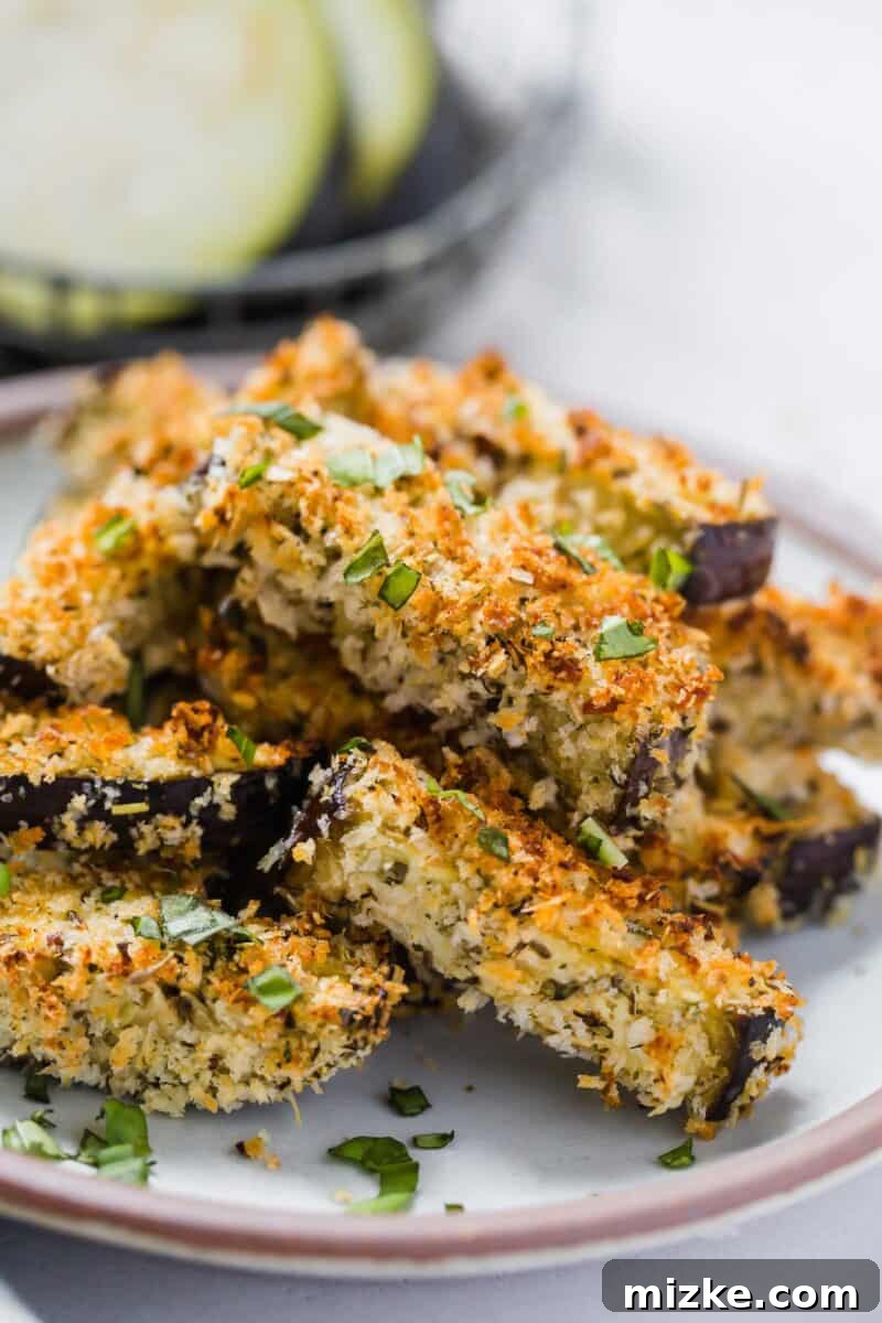 A bowl of crispy Eggplant Parmesan Fries ready to be served, accompanied by a small dish of warm marinara sauce and fresh basil garnish.
