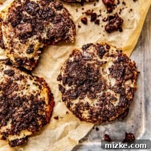 A freshly baked Oreo cheesecake cookie on parchment paper, resting on a metal baking sheet, ready to cool and be savored.