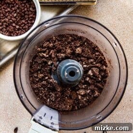 Finely crushed Oreo cookies in a food processor, ready for coating the cheesecake cookie dough.