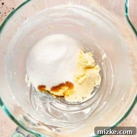 Granulated sugar freshly added to the creamy butter and cream cheese mixture in a stand mixer.