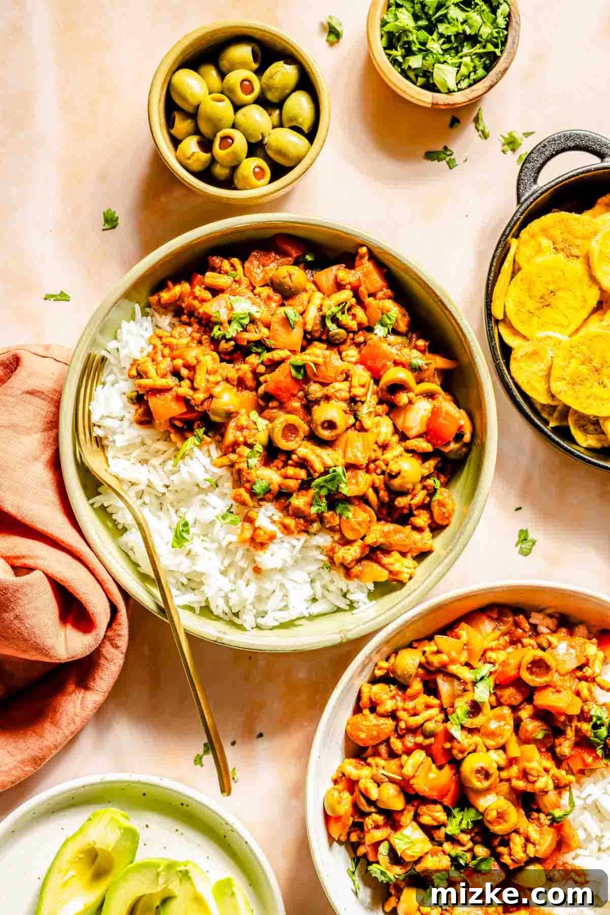 Savory Turkey Picadillo 3 Turkey picadillo on a bed of white rice in a green bowl with a fork laying on its side. The bowl is next to olives and plantain chips, showcasing a complete meal