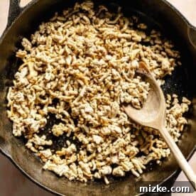 Savory Turkey Picadillo 5 Ground turkey in a cast iron skillet broken into smaller pieces with a wooden spoon, indicating the first step of cooking