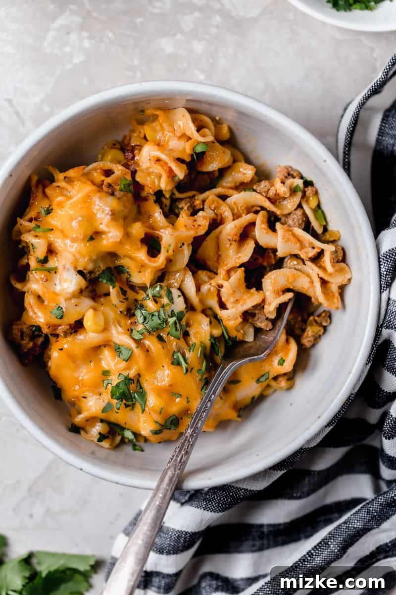 Cheesy Enchilada Pasta Bake 5 A serving of Enchilada Pasta Casserole on a plate, topped with a dollop of sour cream and fresh cilantro.