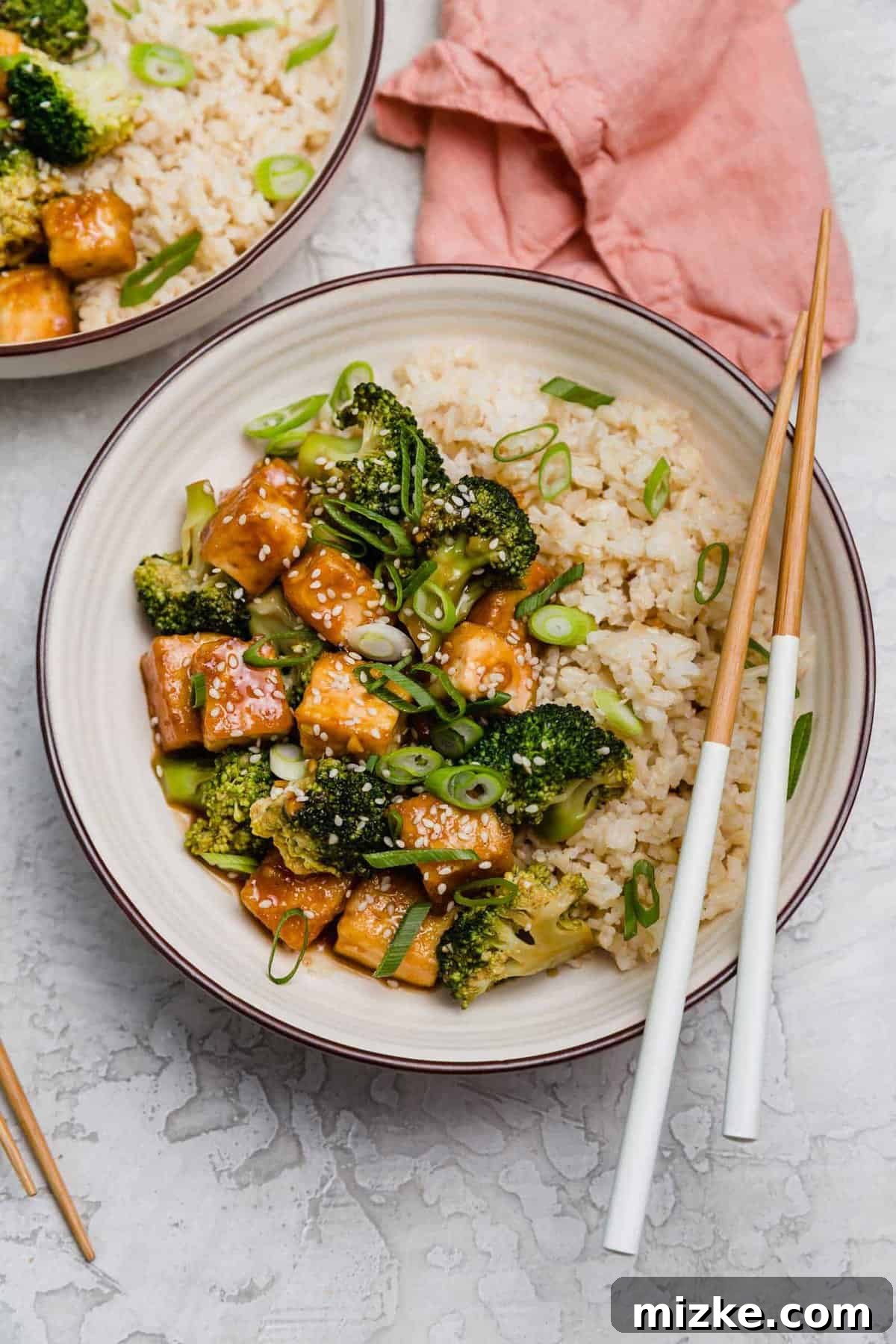 Satisfy your craving for Asian take-out with these teriyaki tofu and broccoli bowls, an easy plant-based dinner for any night of the week! Overhead view of a teriyaki tofu bowl with broccoli, with a pair of chopsticks resting on the edge of the bowl.