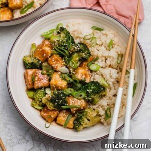 Overhead view of a teriyaki tofu bowl with broccoli, with a pair of chopsticks resting on the edge of the bowl.