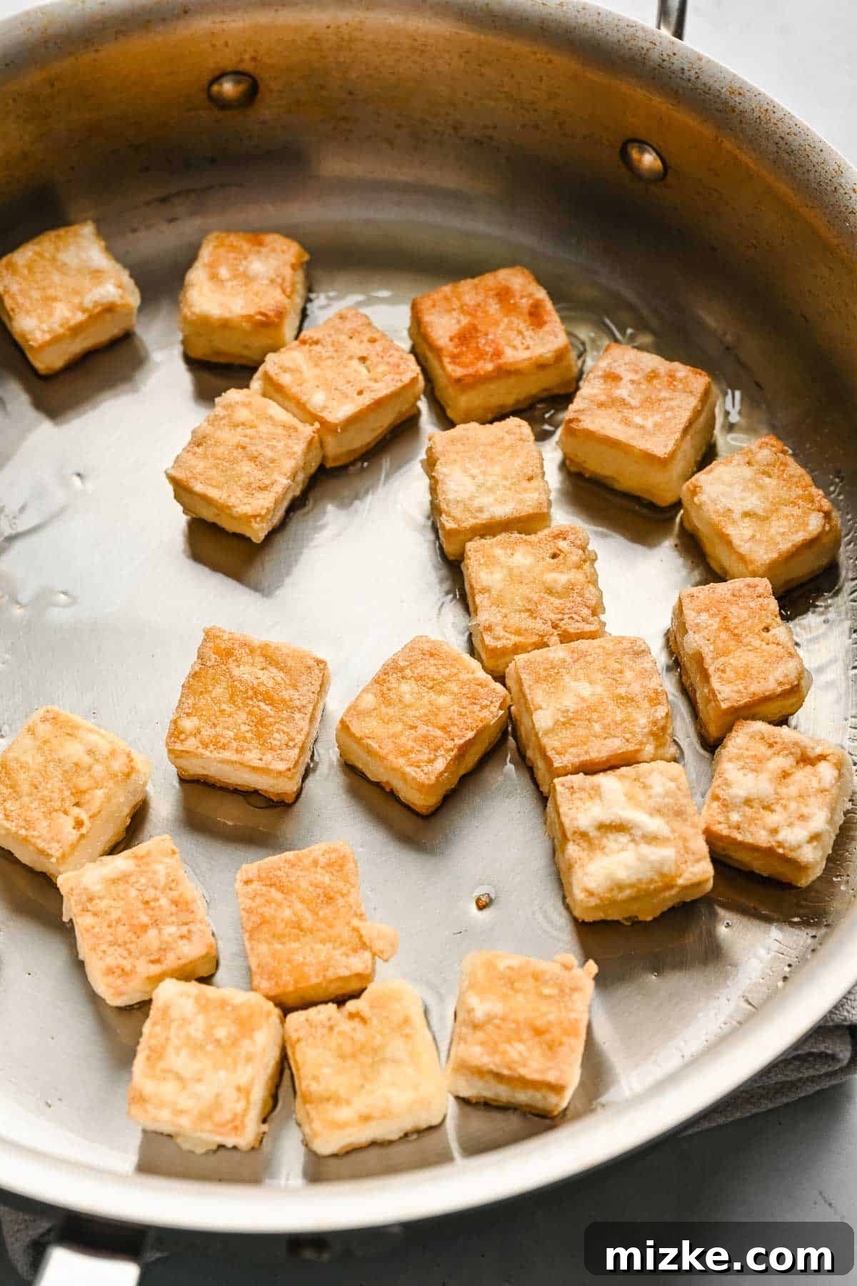 Satisfy your craving for Asian take-out with these teriyaki tofu and broccoli bowls, an easy plant-based dinner for any night of the week! Close up of browned cubed tofu in a metal skillet.