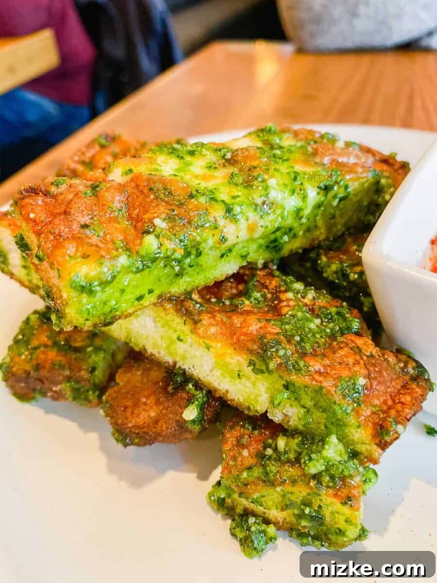 DC Date Night Done Right: Emmy Squared 4 A plate piled high with golden-brown cheesy garlic sticks, generously topped with melted cheese and fresh herbs, showcasing their crispy texture.