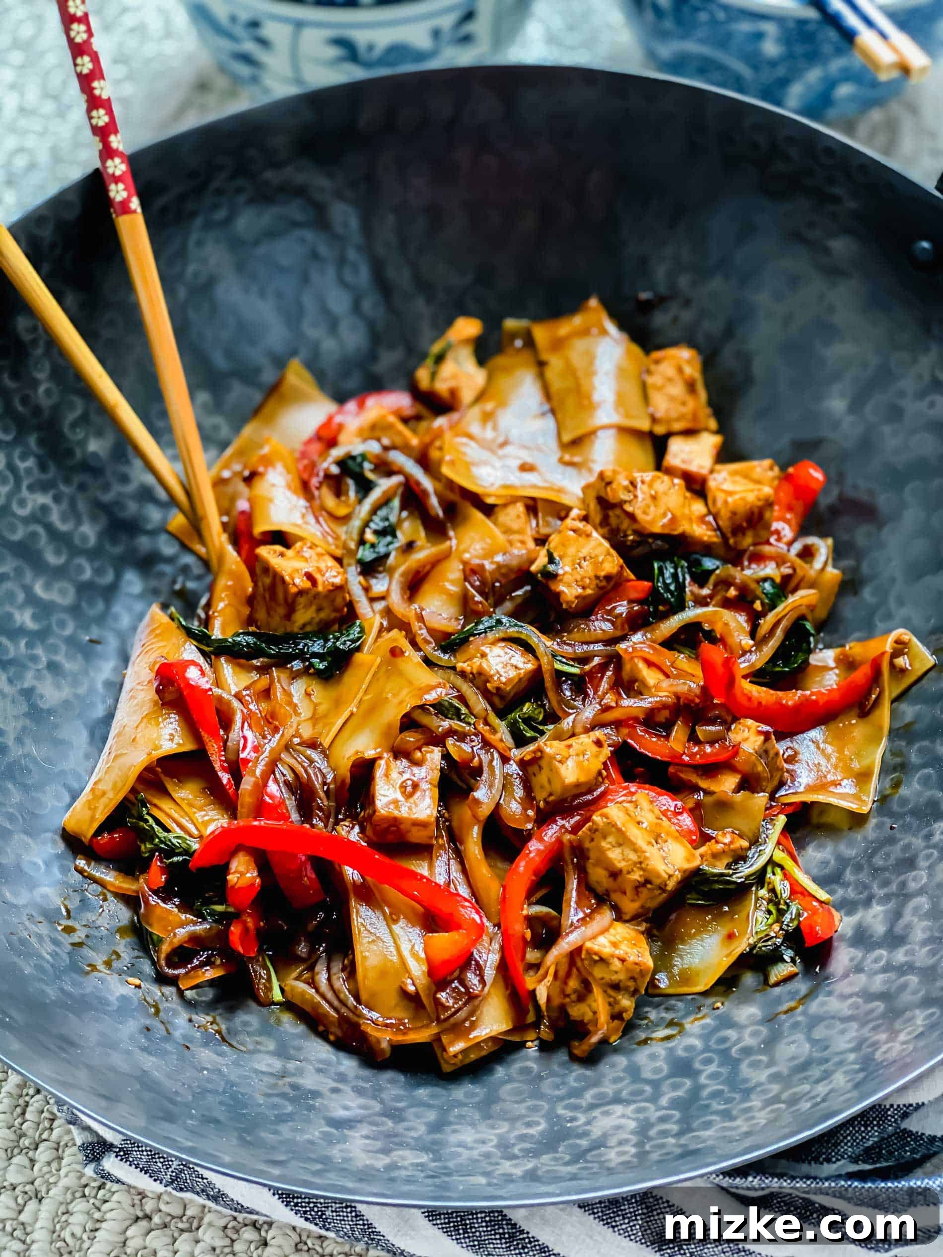 This recipe for drunken noodles with tofu is full of flavor and easy enough for a weeknight. Make your favorite Thai dish right at home! Closeup shot of drunken noodles in wok with chopsticks.