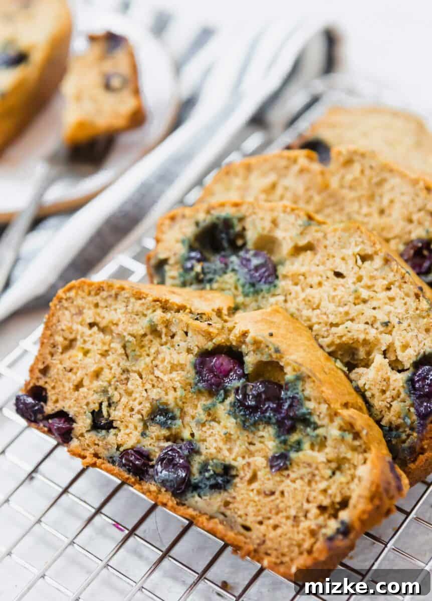 Blueberry Burst Banana Loaf 3 Close-up of a rustic wooden cutting board with a cooling blueberry banana bread loaf, still warm and inviting.