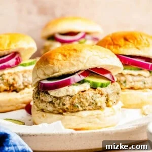A turkey spinach feta burger on a brioche bun with red onion rings, cucumbers, and hummus peeking out of the burger