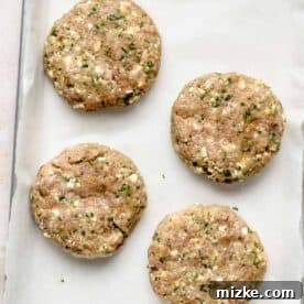 Mediterranean Turkey Spinach Feta Burgers 7 Four perfectly formed turkey spinach feta burger patties arranged on a parchment-lined metal baking sheet, ready for cooking.