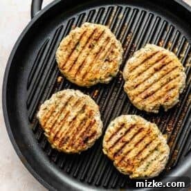 Mediterranean Turkey Spinach Feta Burgers 8 Two turkey spinach feta burgers cooking on a cast iron grill pan, displaying appealing grill marks.